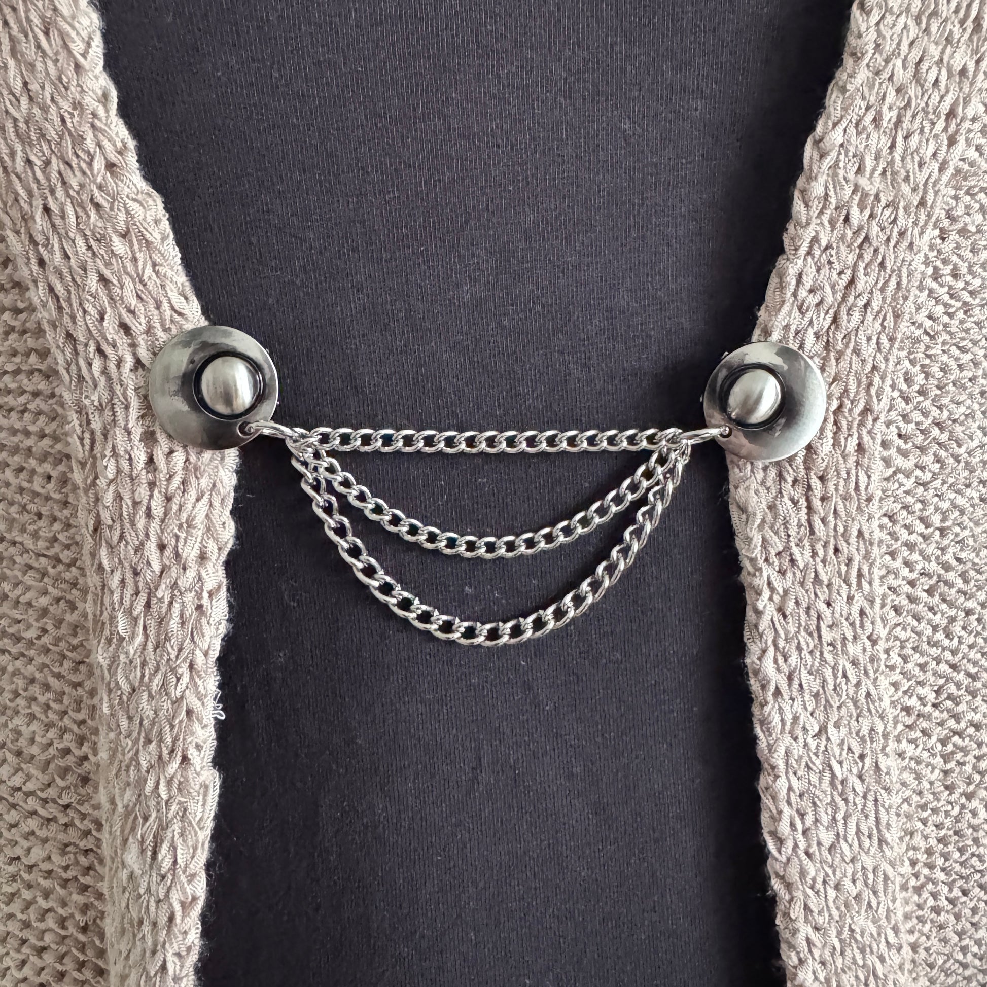 Vestsluiting De Keten 3 zilver gedragen op een grofgebreid vest, elegante Fashionclip met zilverkleurige clips en drievoudige ketting.