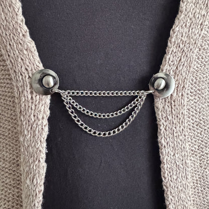 Vestsluiting De Keten 3 zilver gedragen op een grofgebreid vest, elegante Fashionclip met zilverkleurige clips en drievoudige ketting.