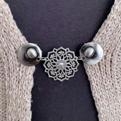 Vestsluiting De Mandala in close-up op een gebreid vest, elegante Fashionclip met zilverkleurige clips en opengewerkte mandala tussenbedel.