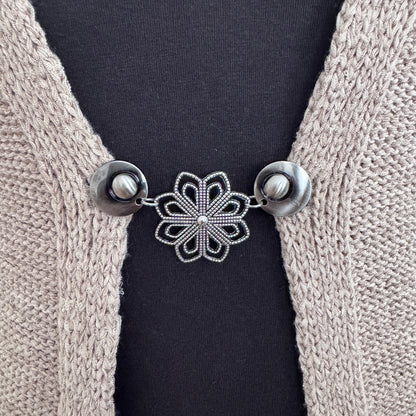 Vestsluiting De Ochtendster in close-up op een gebreid vest, elegante Fashionclip met zilverkleurige clips en bloemvormige tussenbedel.