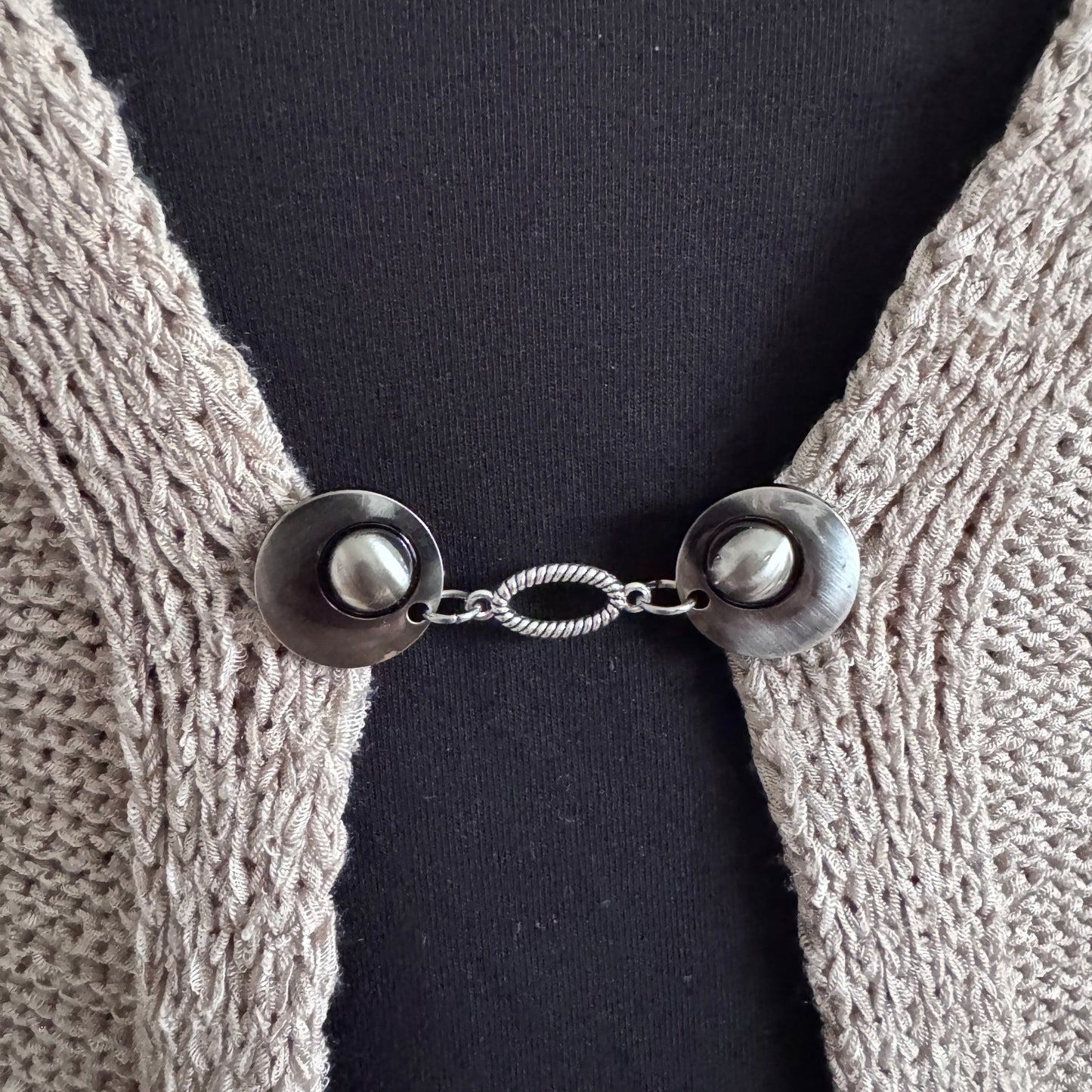 Vestsluiting De Ovaal in close-up op een gebreid vest, elegante Fashionclip met zilverkleurige clips en ovale tussenbedel.