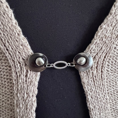 Vestsluiting De Ovaal in close-up op een gebreid vest, elegante Fashionclip met zilverkleurige clips en ovale tussenbedel.