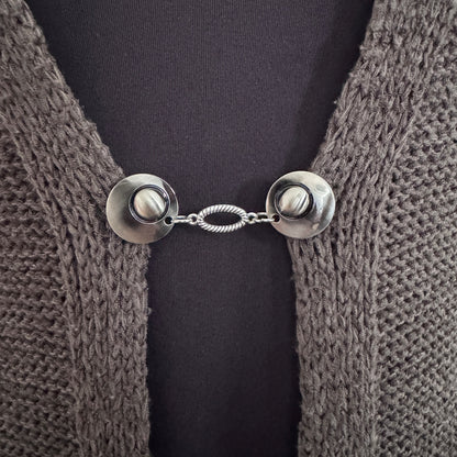 Vestsluiting De Ovaal in close-up op een gebreid vest, elegante Fashionclip met zilverkleurige clips en ovale tussenbedel.