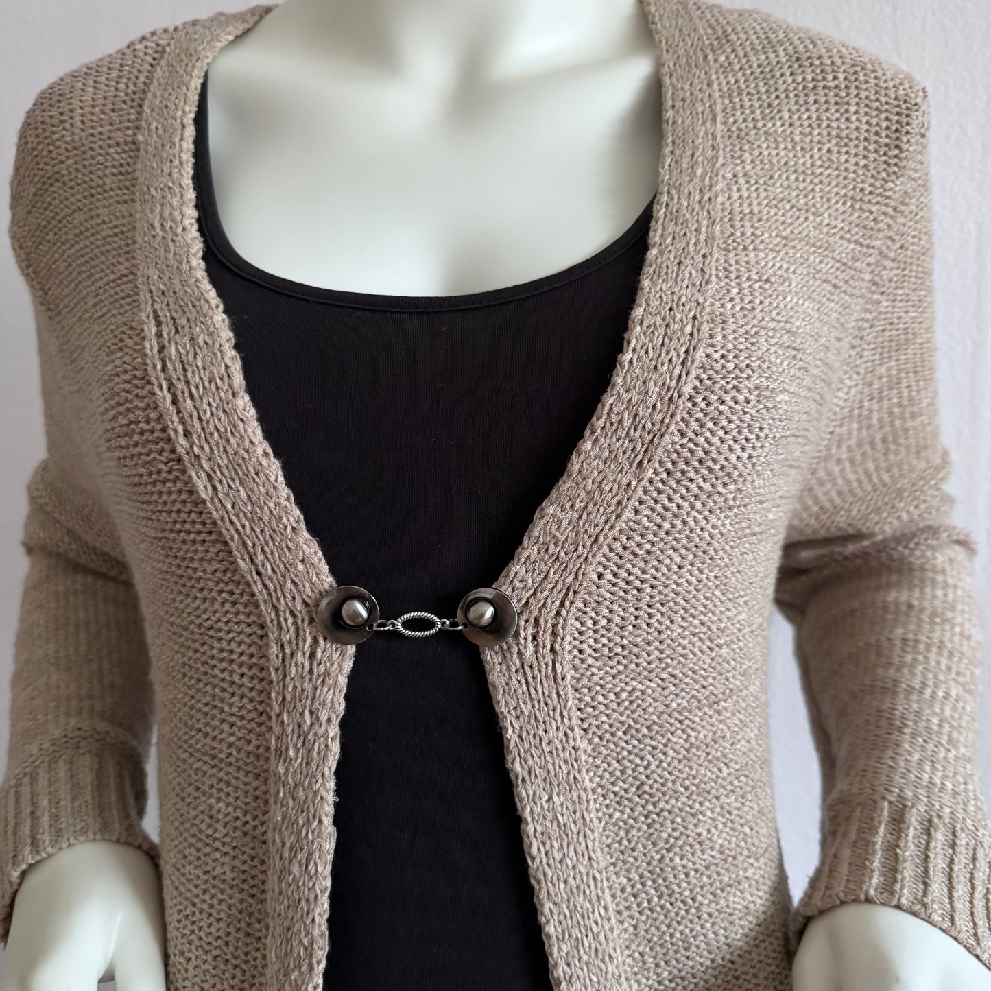 Vestsluiting De Ovaal gedragen op een beige gebreid vest, elegante Fashionclip met zilverkleurige clips en ovale tussenbedel.