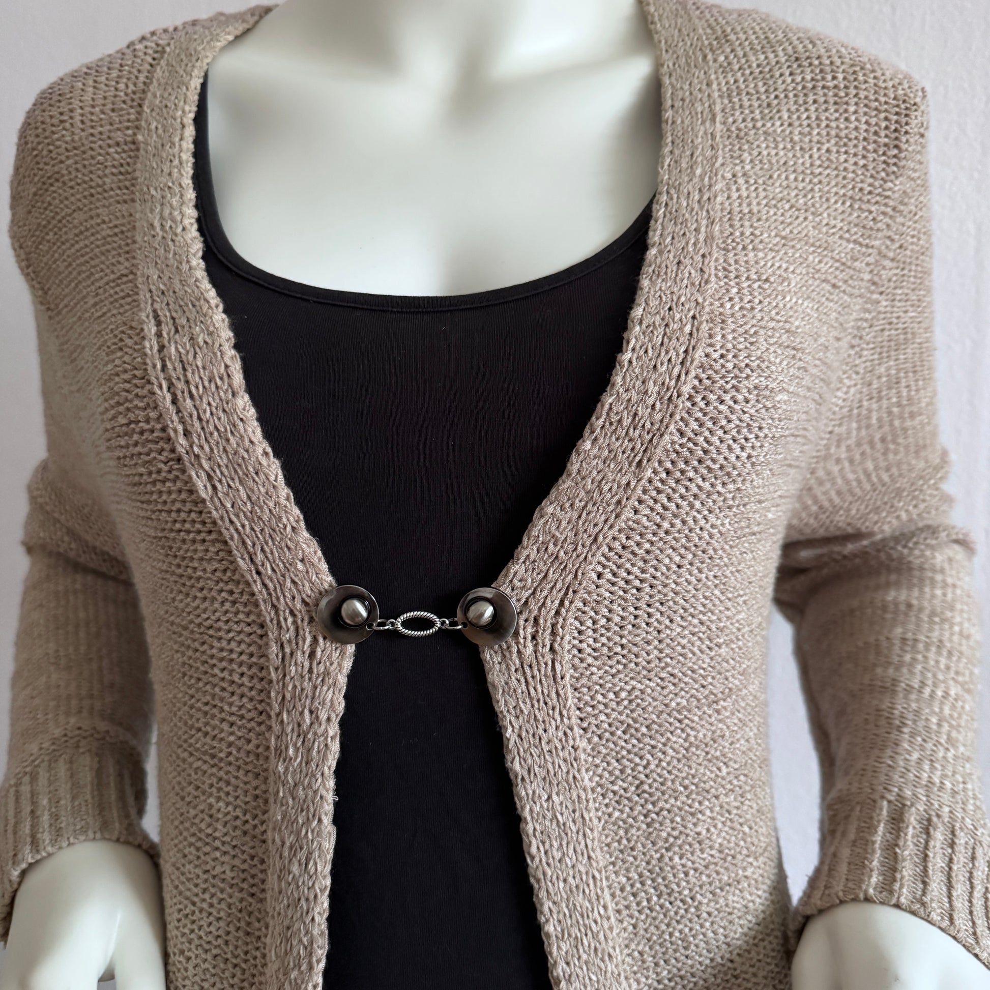 Vestsluiting De Ovaal gedragen op een beige gebreid vest, elegante Fashionclip met zilverkleurige clips en ovale tussenbedel.