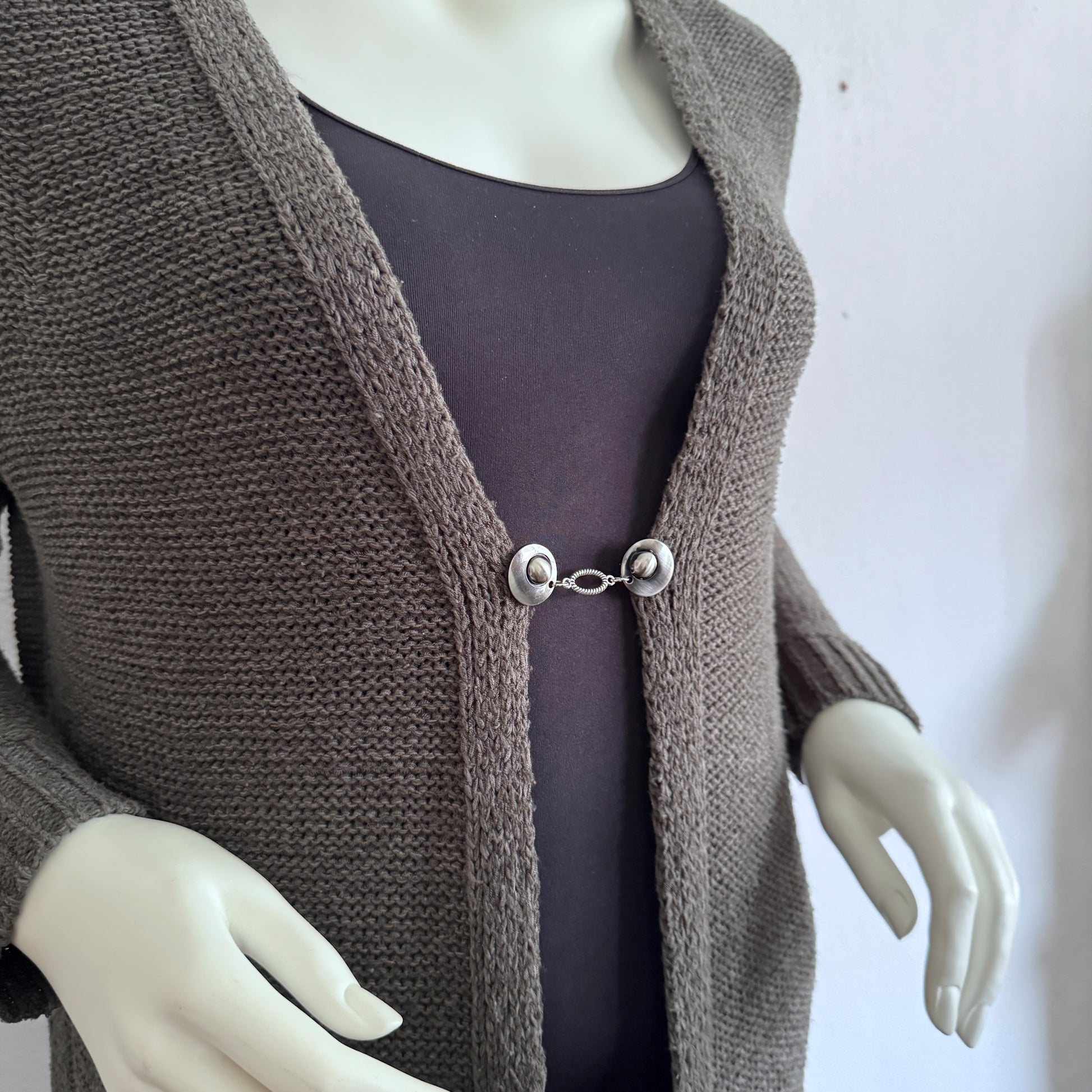 Vestsluiting De Ovaal gedragen op een taupekleurig gebreid vest, elegante Fashionclip met zilverkleurige clips en ovale tussenbedel.