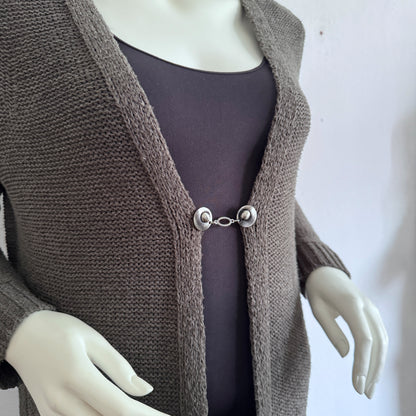 Vestsluiting De Ovaal gedragen op een taupekleurig gebreid vest, elegante Fashionclip met zilverkleurige clips en ovale tussenbedel.