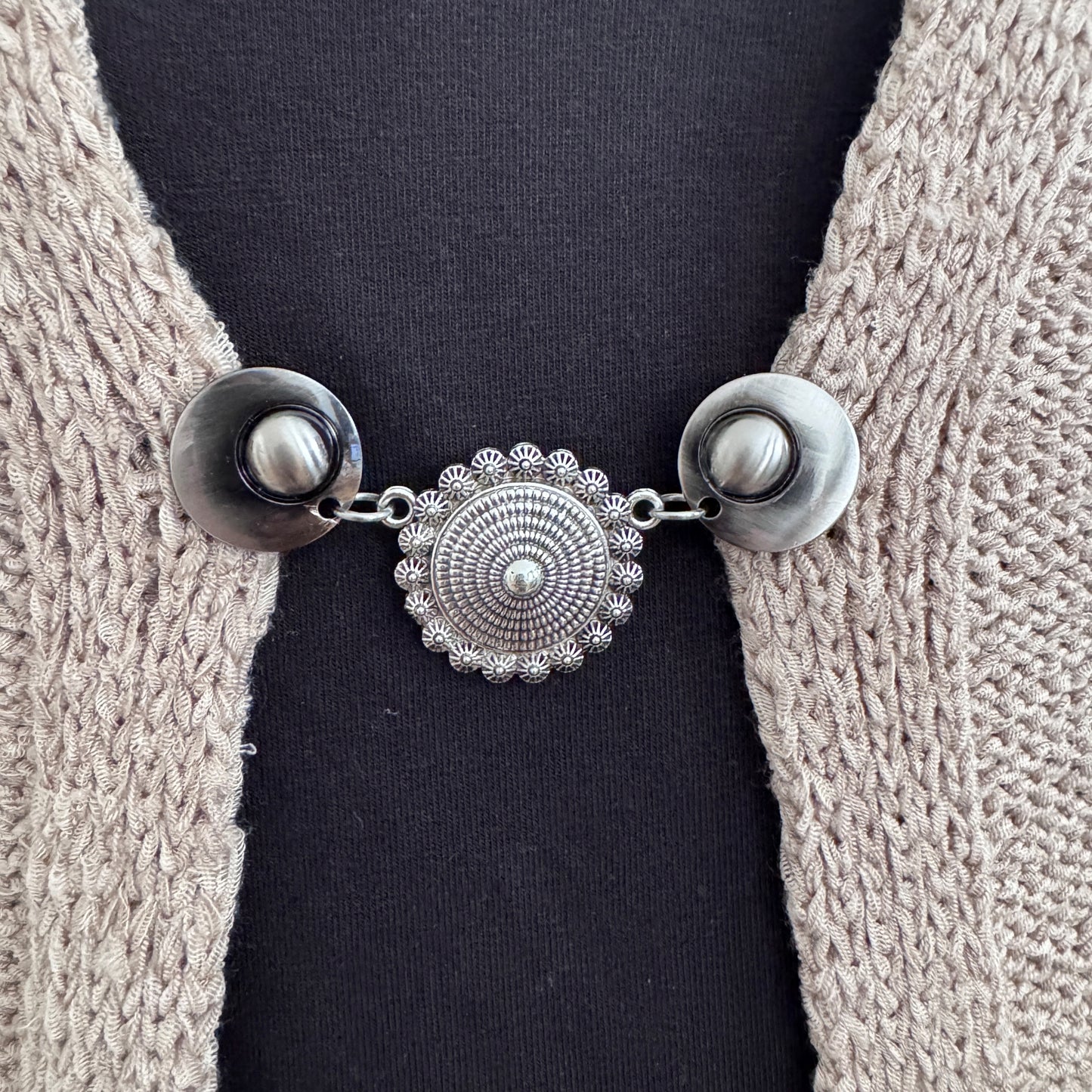 Vestsluiting De Pracht van Zeeland in close-up op een gebreid vest, elegante Fashionclip met zilverkleurige clips en Zeeuwse knop tussenbedel.