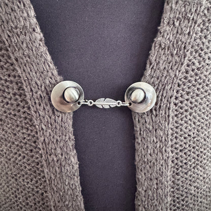 Vestsluiting De Veer in close-up op een gebreid vest, elegante Fashionclip met zilverkleurige clips en verfijnde veer tussenbedel.