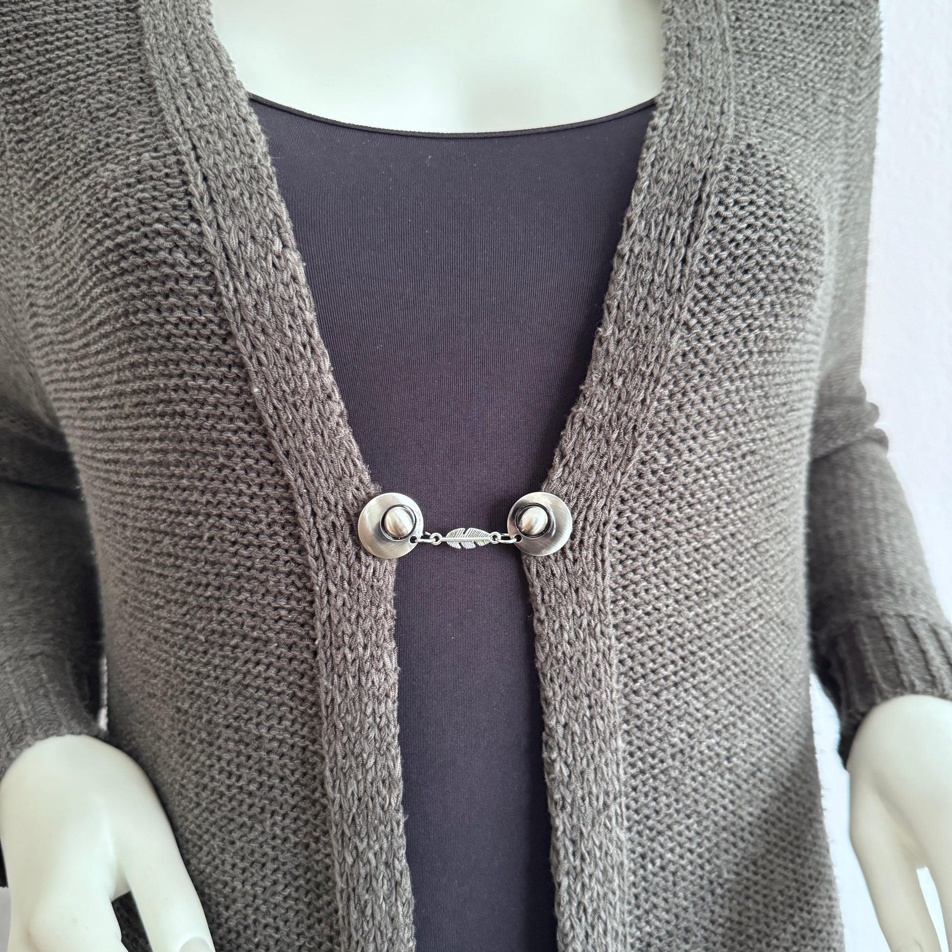 Vestsluiting De Veer gedragen op een gebreid vest, elegante Fashionclip met zilverkleurige clips en verfijnde veerbedel.