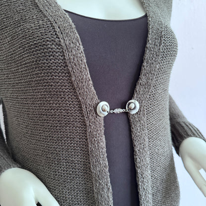 Vestsluiting De Veer gedragen op een taupekleurig gebreid vest, elegante Fashionclip met zilverkleurige clips en verfijnde veer tussenbedel.