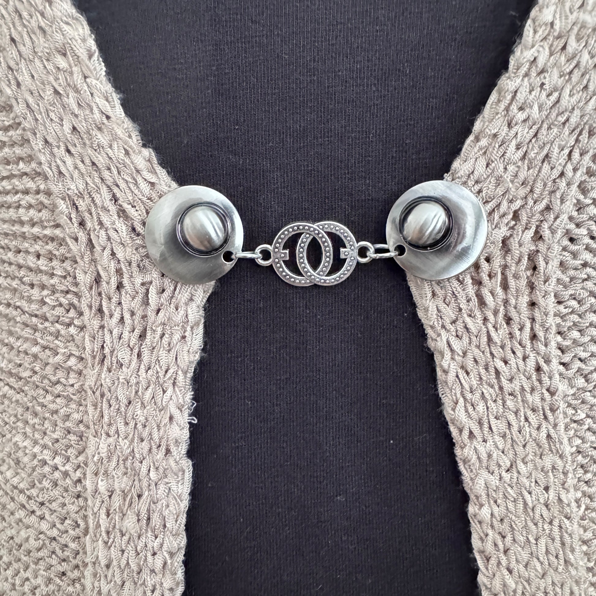 Vestsluiting De Verbinding in close-up op een gebreid vest, elegante Fashionclip met zilverkleurige clips en verbonden cirkelvormige tussenbedel.