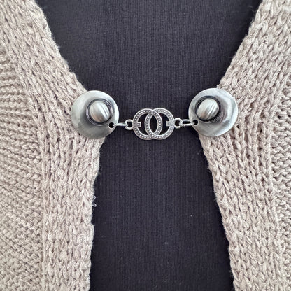Vestsluiting De Verbinding in close-up op een gebreid vest, elegante Fashionclip met zilverkleurige clips en verbonden cirkelvormige tussenbedel.