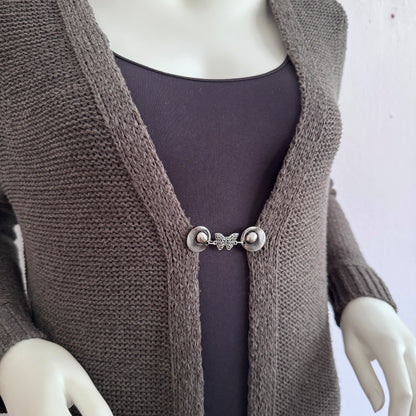 Vestsluiting De Vlinder gedragen op een taupekleurig gebreid vest, elegante Fashionclip met zilverkleurige clips en vlindervormige tussenbedel.