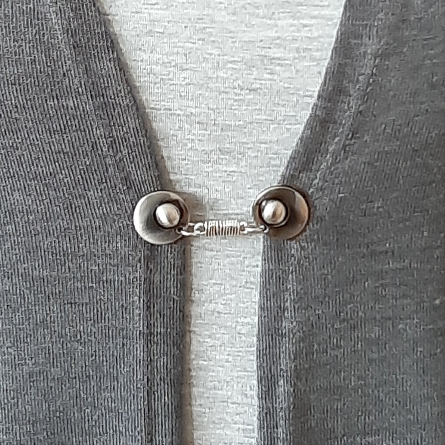 Vestsluiting De Wikkeling gedragen op een grijs vest, elegante Fashionclip met zilverkleurige clips en verfijnde wikkelverbinding.