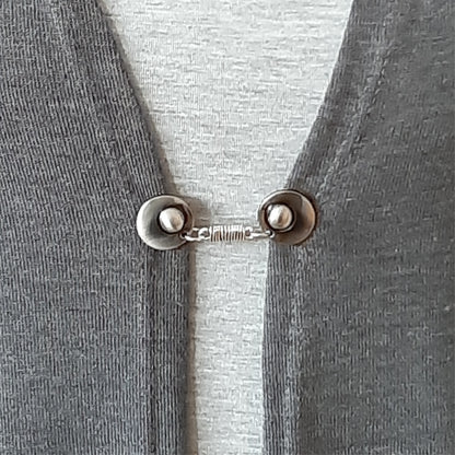 Vestsluiting De Wikkeling gedragen op een grijs vest, elegante Fashionclip met zilverkleurige clips en verfijnde wikkelverbinding.