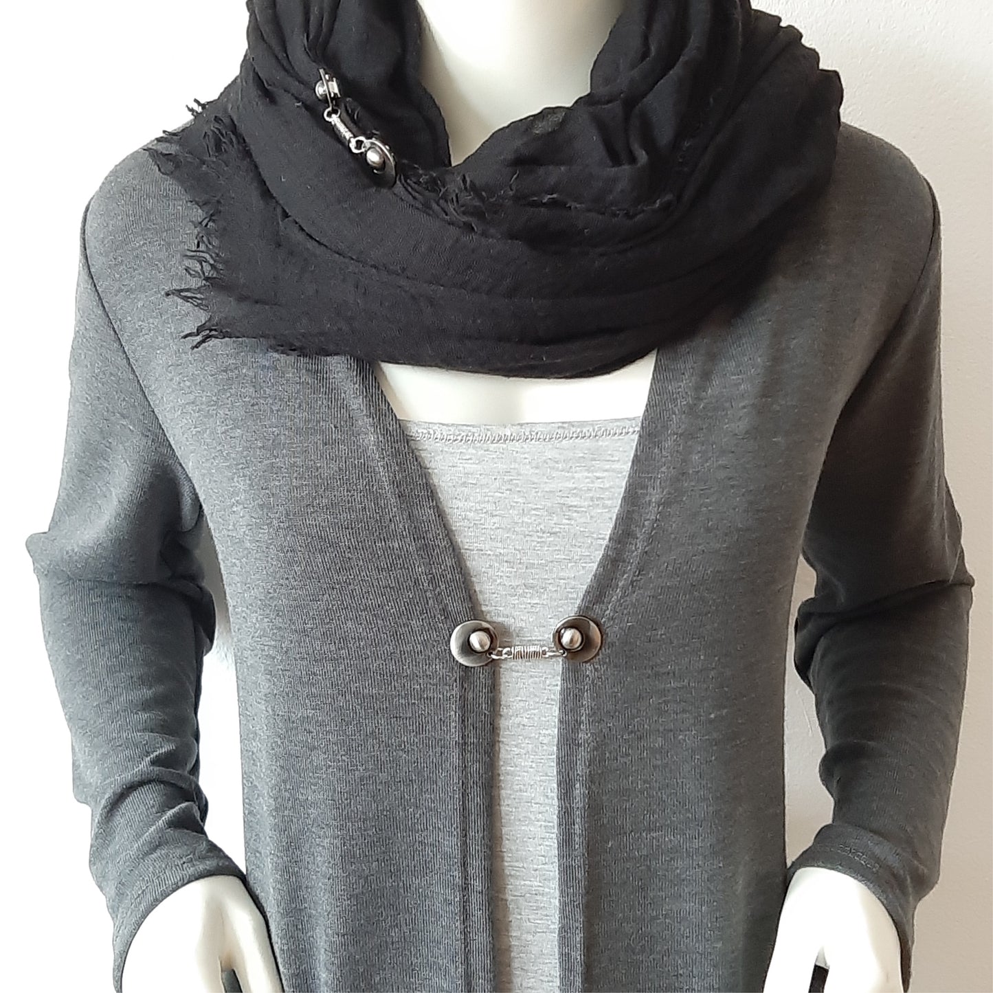 Vestsluiting De Wikkeling gedragen op een grijs vest met zwarte sjaal, elegante Fashionclip met zilverkleurige clips en verfijnde wikkelverbinding.