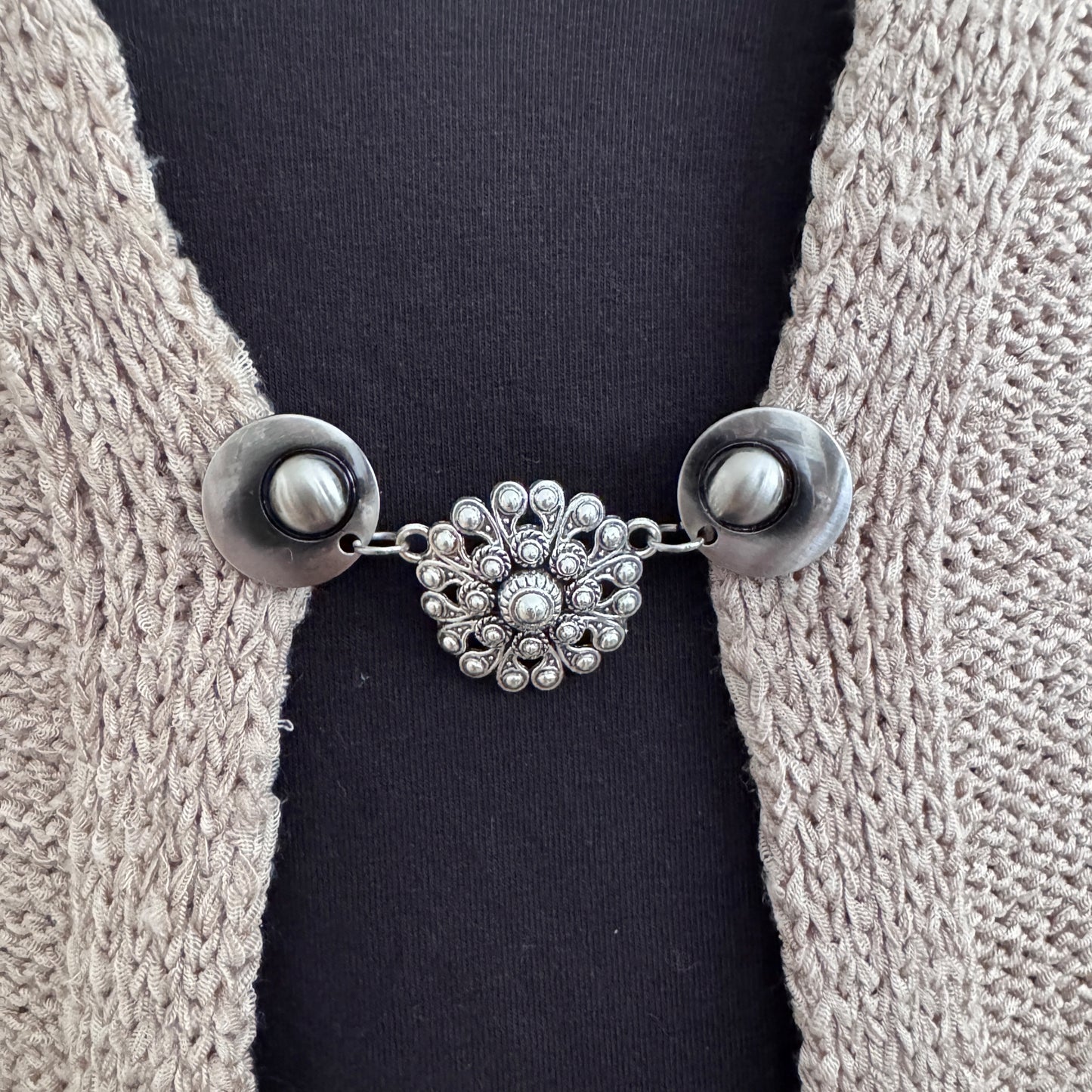 Vestsluiting De Zeeuwse Knoop in close-up op een gebreid vest, elegante Fashionclip met zilverkleurige clips en Zeeuwse knop tussenbedel.
