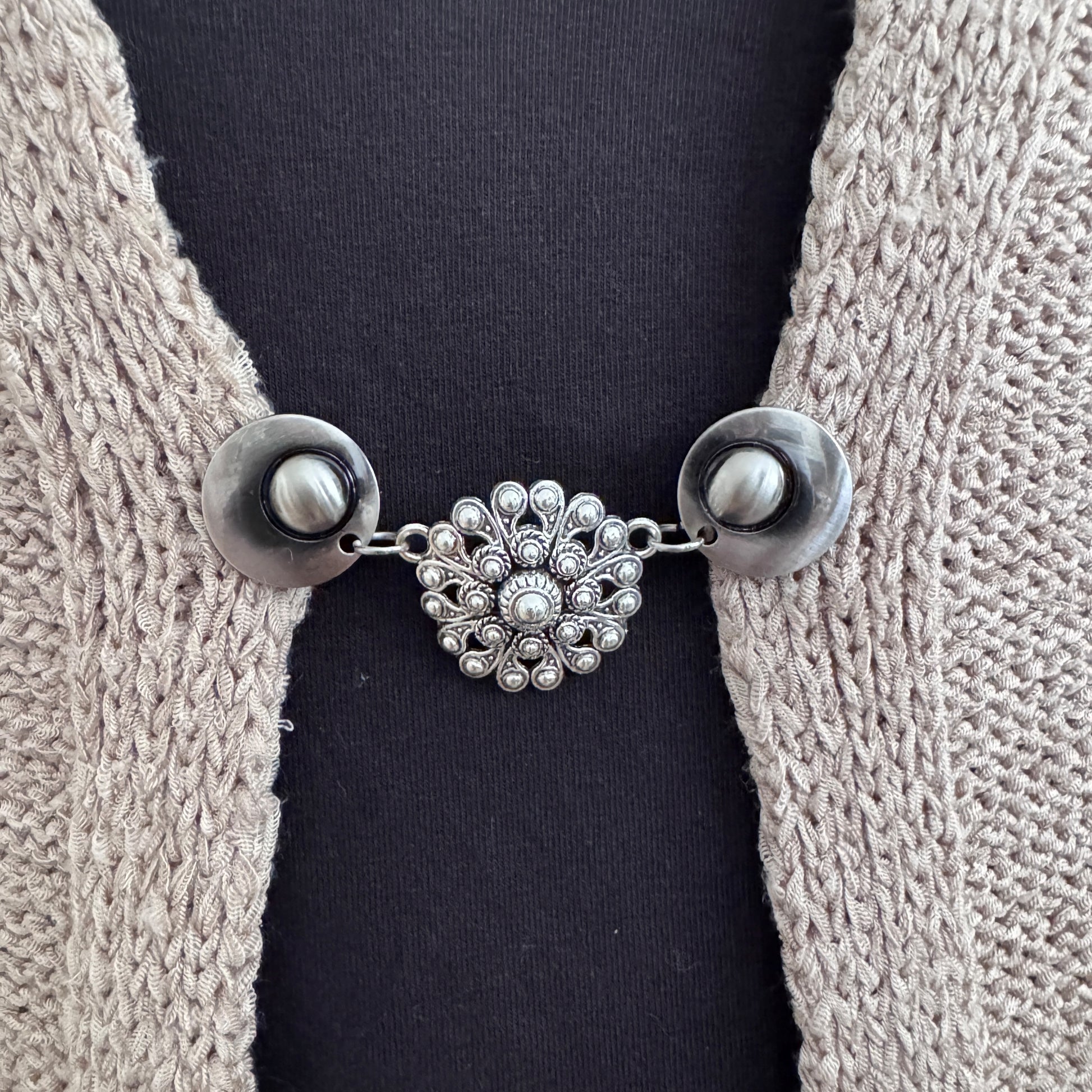 Vestsluiting De Zeeuwse Knoop in close-up op een gebreid vest, elegante Fashionclip met zilverkleurige clips en Zeeuwse knop tussenbedel.