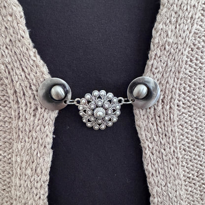 Vestsluiting De Zeeuwse Knoop in close-up op een gebreid vest, elegante Fashionclip met zilverkleurige clips en Zeeuwse knop tussenbedel.