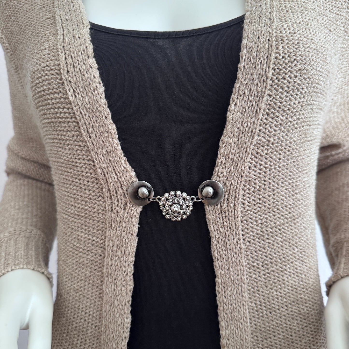 Vestsluiting De Zeeuwse Knoop gedragen op een beige gebreid vest, elegante Fashionclip met zilverkleurige clips en Zeeuwse knop tussenbedel.