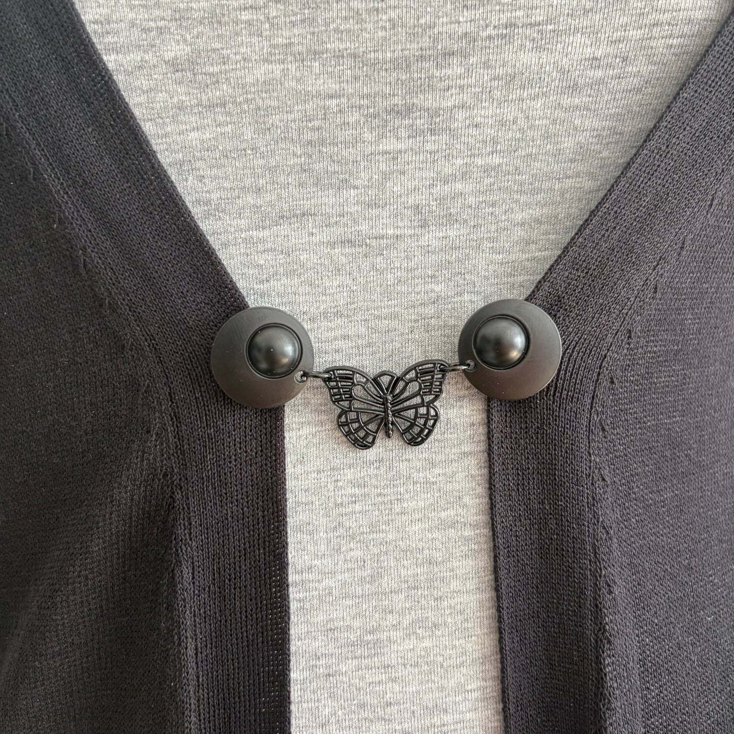 Vestsluiting De Zwarte Vlinder in close-up op een donker vest, elegante Fashionclip met matzwarte clips en opengewerkte vlinderbedel.