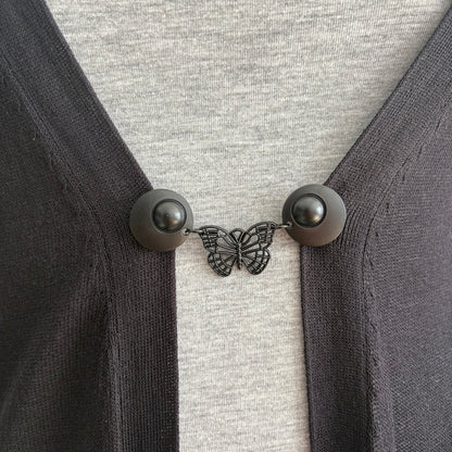 Vestsluiting De Zwarte Vlinder in close-up op een donker vest, elegante Fashionclip met matzwarte clips en opengewerkte vlinderbedel.