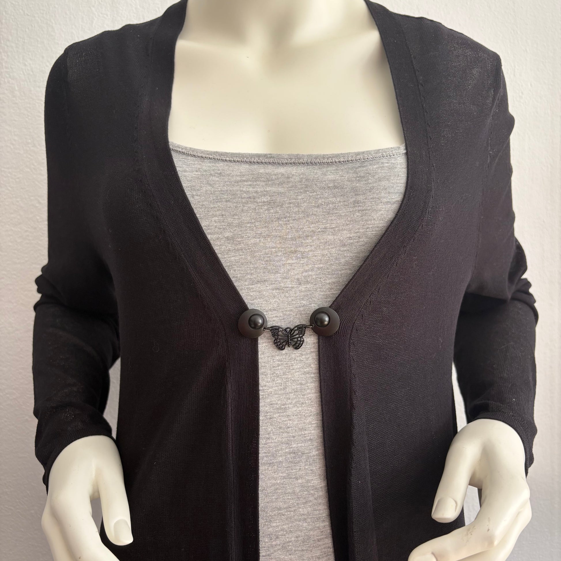 Vestsluiting De Zwarte Vlinder gedragen op een zwart vest met grijze top, elegante Fashionclip met matzwarte clips en vlindervormige tussenbedel.