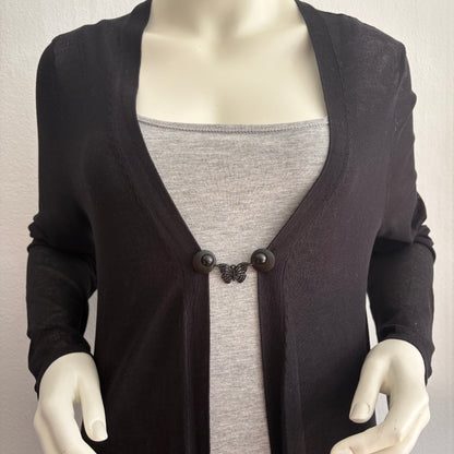 Vestsluiting De Zwarte Vlinder gedragen op een zwart vest met grijze top, elegante Fashionclip met matzwarte clips en vlindervormige tussenbedel.