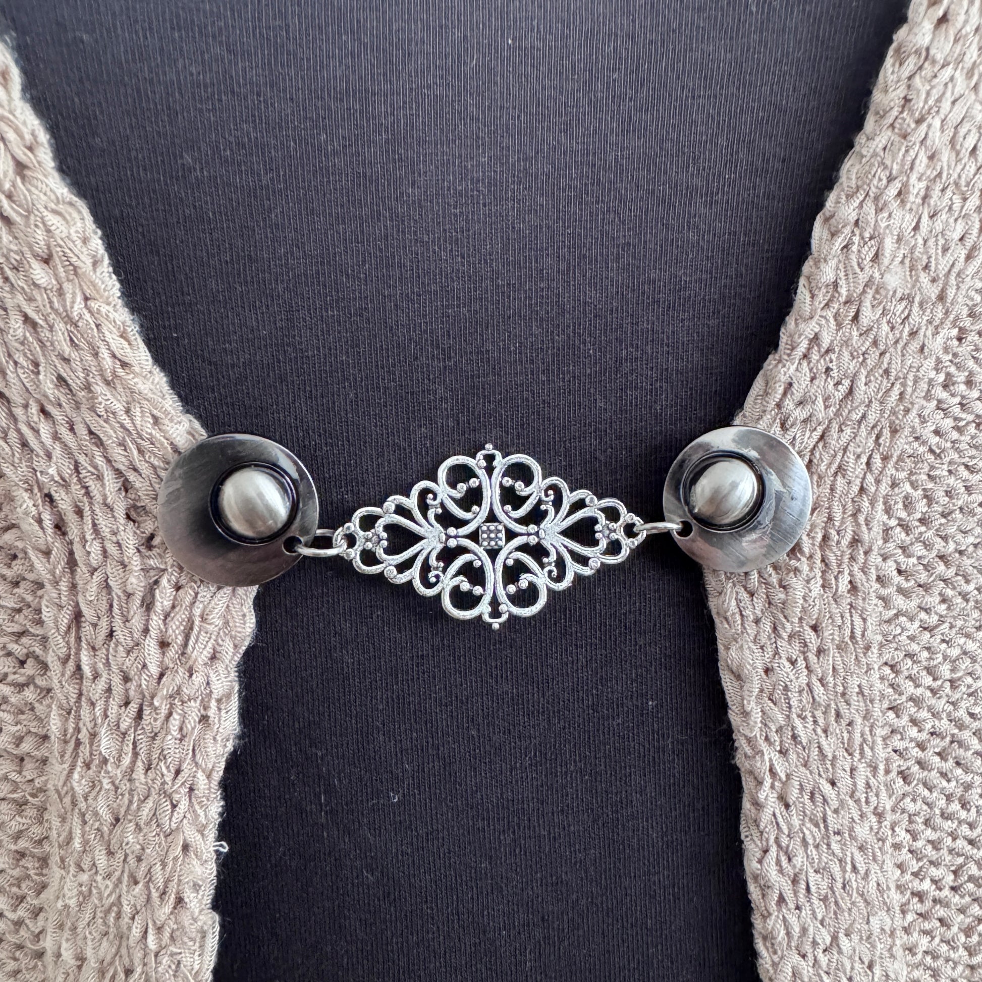 Vestsluiting Frans Brocante zilver in close-up op een gebreid vest, elegante Fashionclip met zilverkleurige clips en sierlijke brocante tussenbedel.