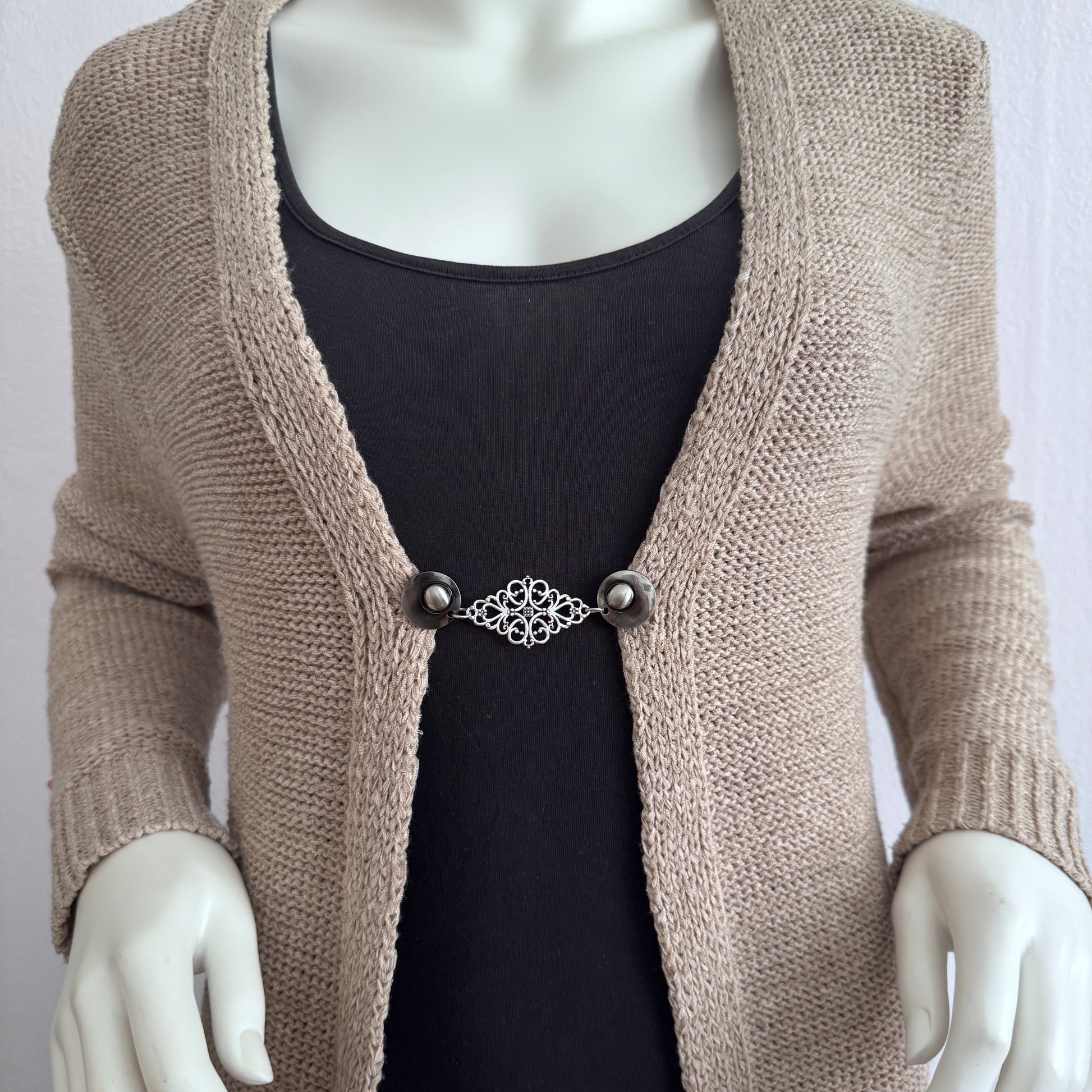 Vestsluiting Frans Brocante zilver gedragen op een beige gebreid vest, elegante Fashionclip met zilverkleurige clips en sierlijke brocante tussenbedel.