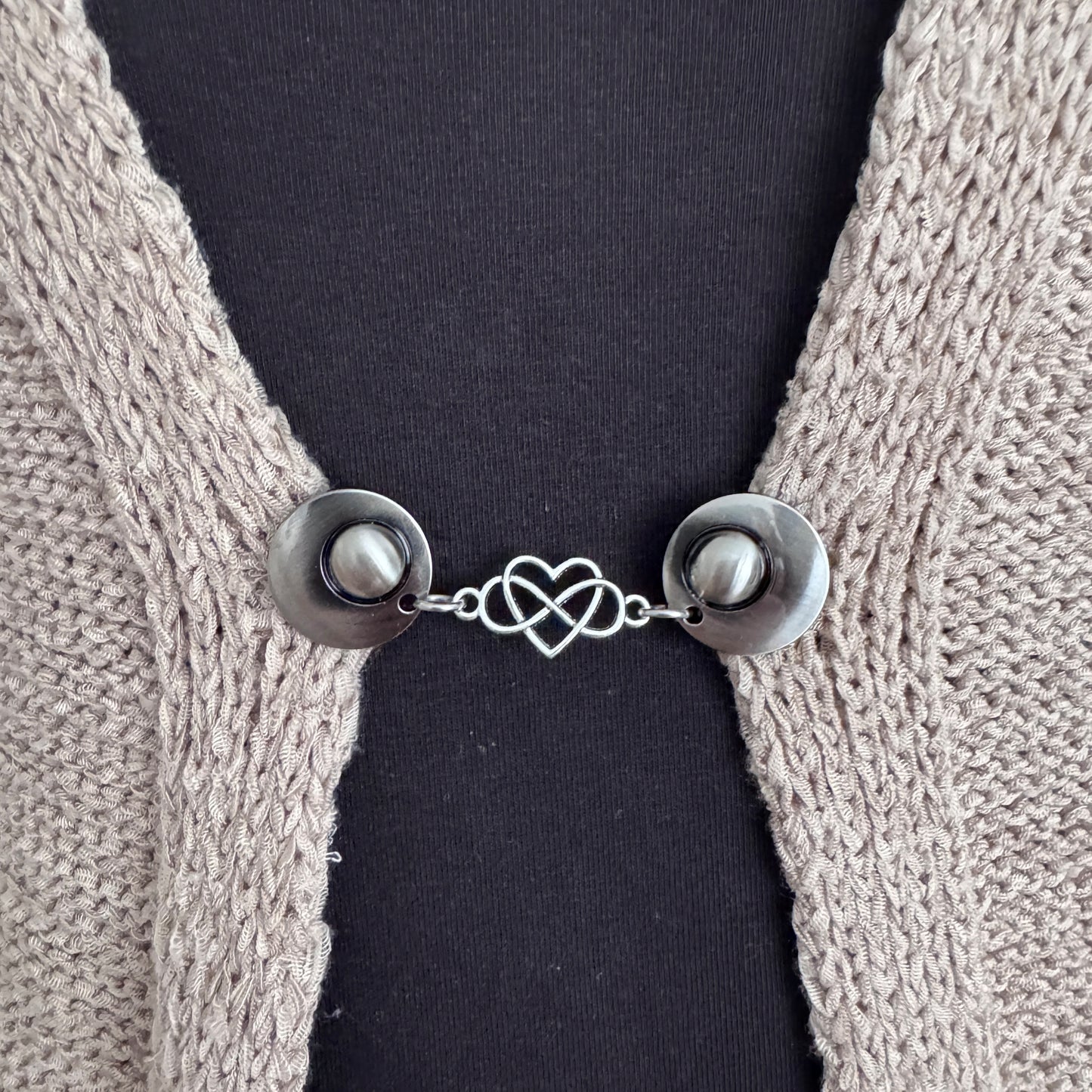Vestsluiting Het Hart in close-up op een gebreid vest, elegante Fashionclip met zilverkleurige clips en hartvormige tussenbedel.