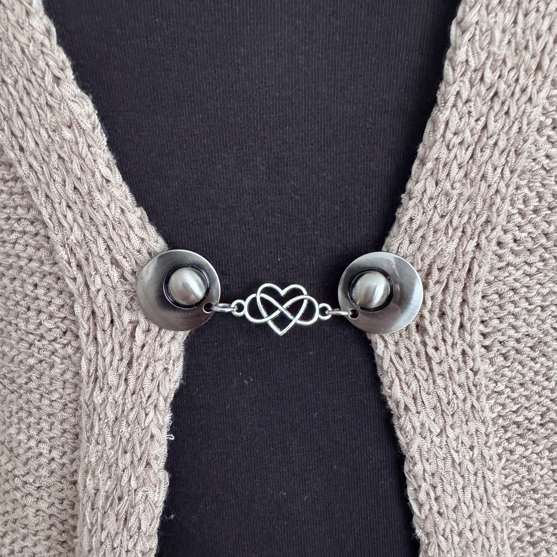 Vestsluiting Het Hart in close-up op een gebreid vest, elegante Fashionclip met zilverkleurige clips en hartvormige tussenbedel.