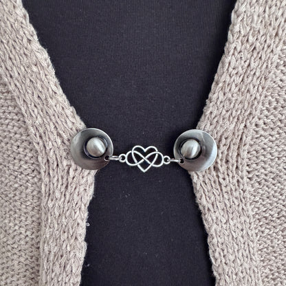 Vestsluiting Het Hart in close-up op een gebreid vest, elegante Fashionclip met zilverkleurige clips en hartvormige tussenbedel.