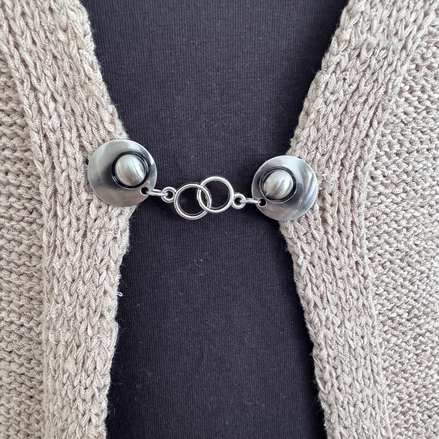 Vestsluiting Het Houvastje in close-up op een gebreid vest, elegante Fashionclip met zilverkleurige clips en dubbele ringverbinding.