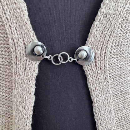 Vestsluiting Het Houvastje in close-up op een gebreid vest, elegante Fashionclip met zilverkleurige clips en dubbele ringverbinding.