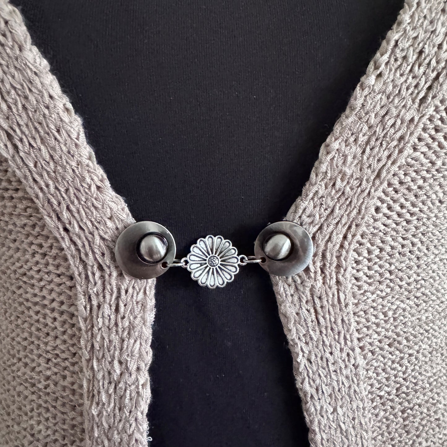 Vestsluiting Het Madeliefje in close-up op een gebreid vest, elegante Fashionclip met zilverkleurige clips en madeliefvormige tussenbedel.