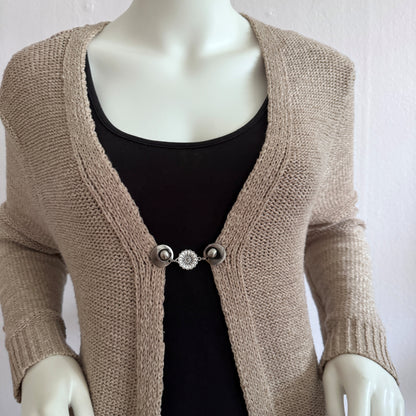 Vestsluiting Het Madeliefje gedragen op een beige gebreid vest, elegante Fashionclip met zilverkleurige clips en madeliefvormige tussenbedel.