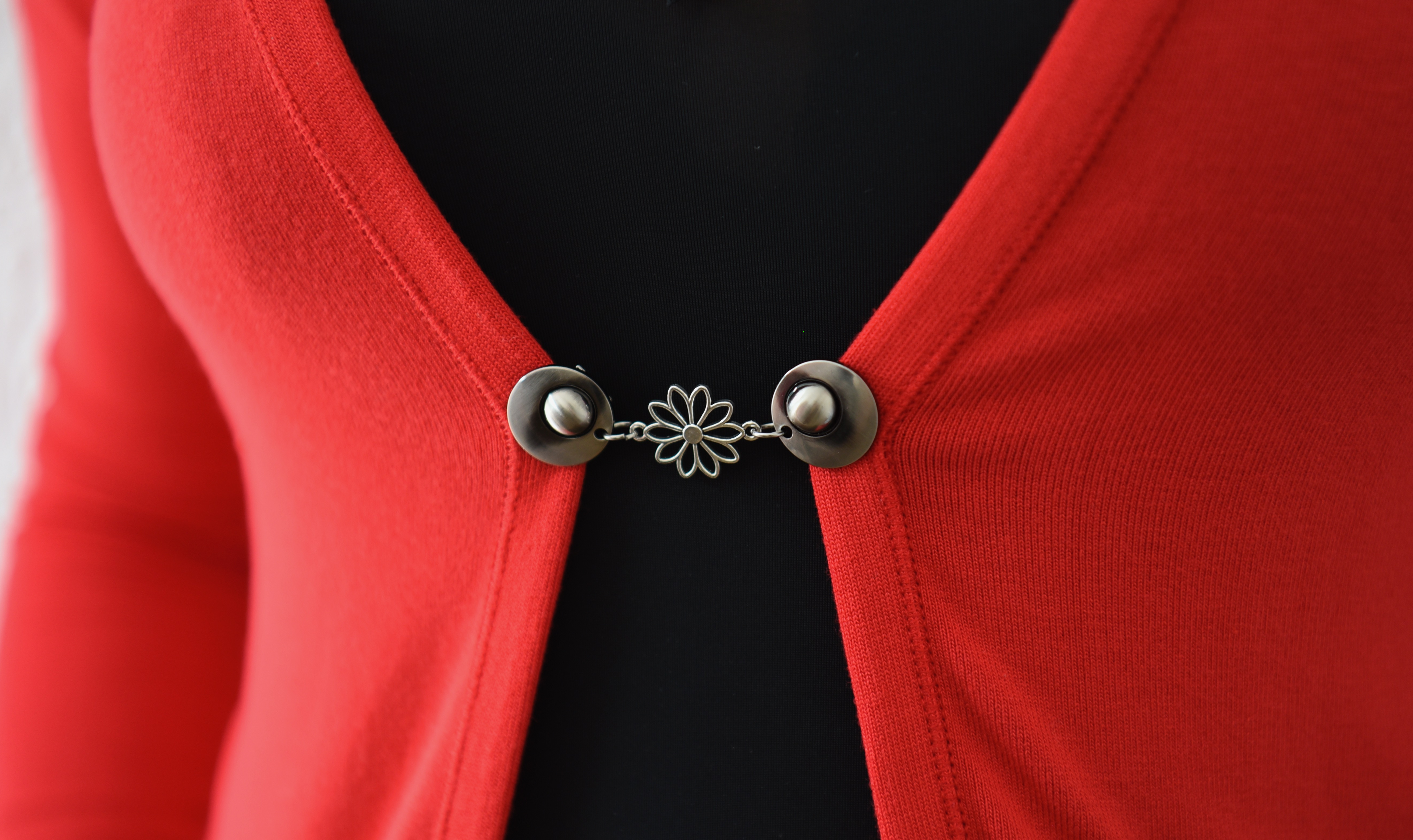 Vestsluiting Het Madeliefje zilver bevestigd op een rood vest, met elegante clips en bloemvormige tussenbedel voor een vrolijke en vrouwelijke uitstraling.