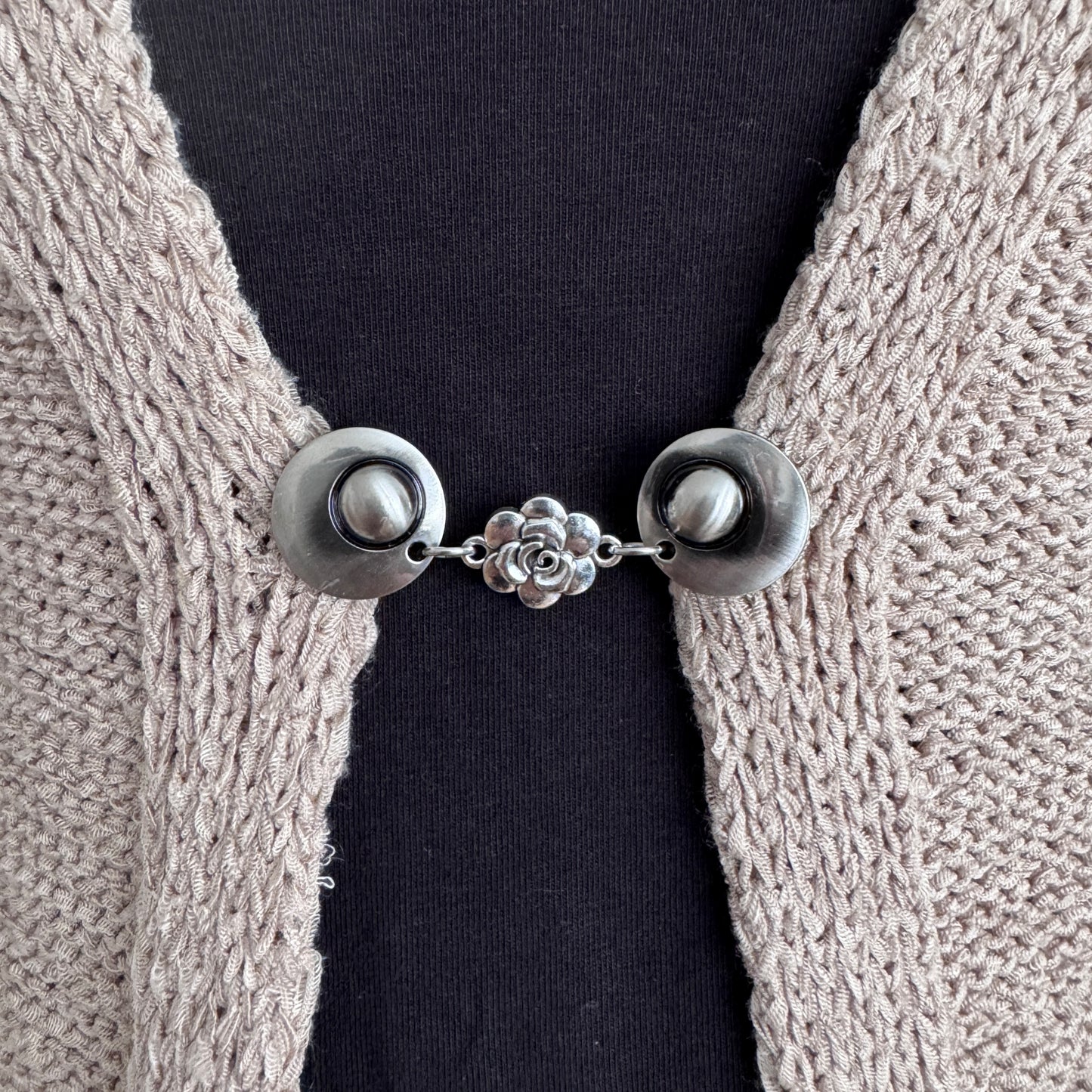 Vestsluiting Het Roosje in close-up op een gebreid vest, elegante Fashionclip met zilverkleurige clips en roosvormige tussenbedel.