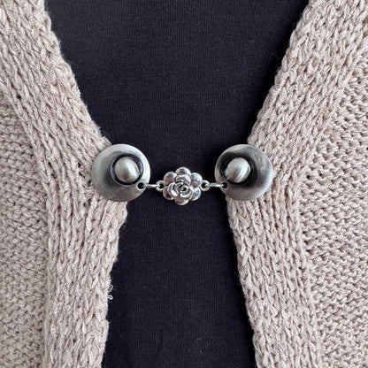 Vestsluiting Het Roosje in close-up op een gebreid vest, elegante Fashionclip met zilverkleurige clips en roosvormige tussenbedel.