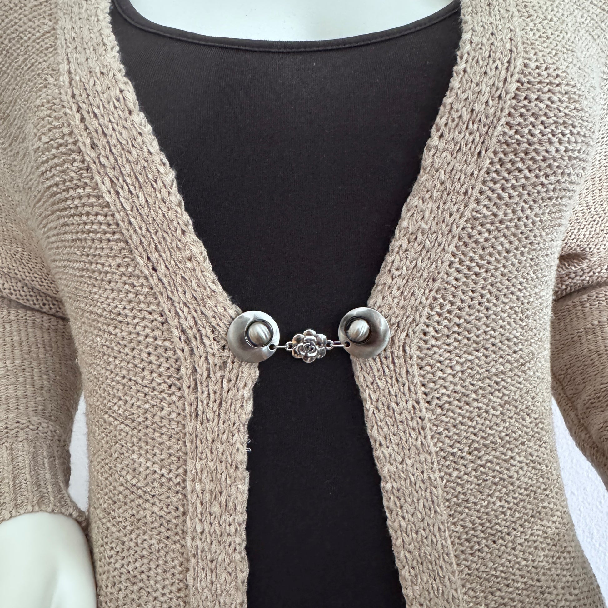 Vestsluiting Het Roosje gedragen op een beige gebreid vest, elegante Fashionclip met zilverkleurige clips en roosvormige tussenbedel.