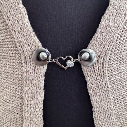 Vestsluiting Het Sprankelende Hart in close-up op een gebreid vest, elegante Fashionclip met zilverkleurige clips en hartvormige tussenbedel met strass.