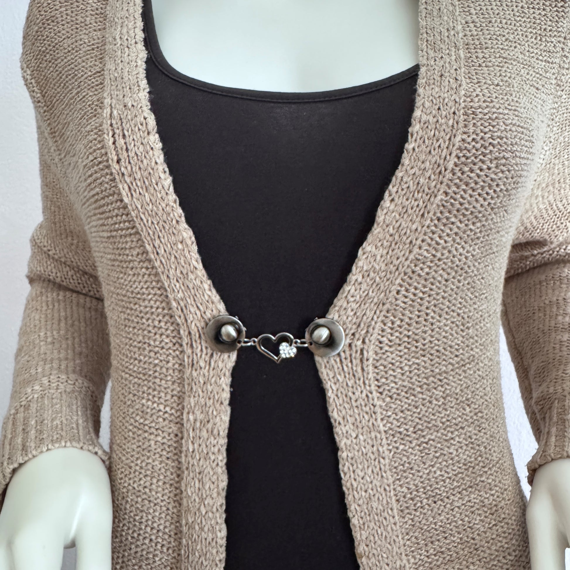 Vestsluiting Het Sprankelende Hart gedragen op een beige gebreid vest, elegante Fashionclip met zilverkleurige clips en hartvormige tussenbedel met strass.