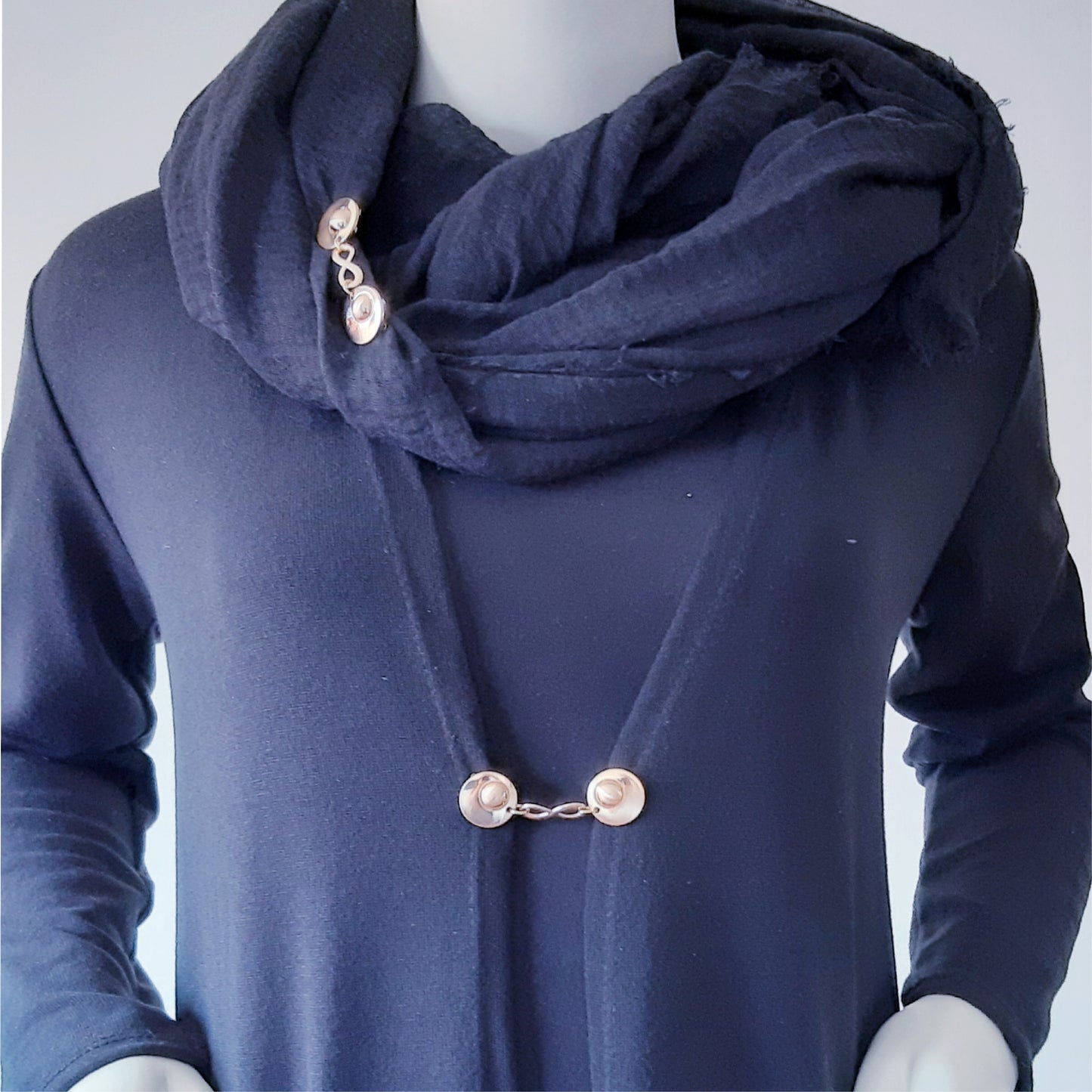 Vestsluiting Infinity goud gedragen op een donkerblauw vest met bijpassende sjaal, elegante Fashionclip met goudkleurige clips en infinity tussenbedel.