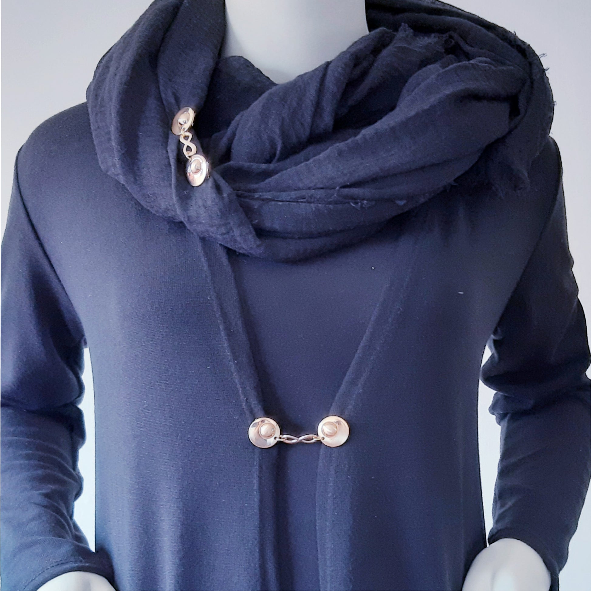 Vestsluiting Infinity goud gedragen op een donkerblauw vest met bijpassende sjaal, elegante Fashionclip met goudkleurige clips en infinity tussenbedel.