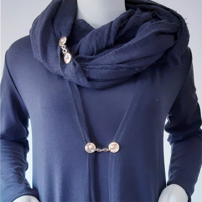 Vestsluiting Infinity goud gedragen op een donkerblauw vest met bijpassende sjaal, elegante Fashionclip met goudkleurige clips en infinity tussenbedel.