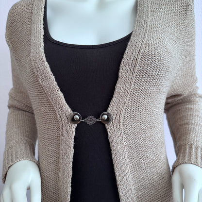 Vestsluiting Kanten Bloem gedragen op een beige gebreid vest, elegante Fashionclip met zilverkleurige clips en verfijnde bloemvormige tussenbedel.