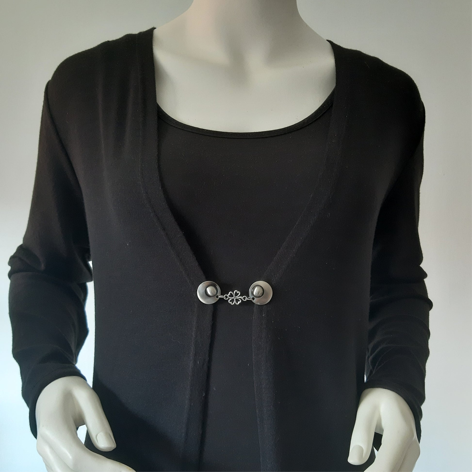 Vestsluiting Klavertje Vier gedragen op een zwart vest, elegante Fashionclip met zilverkleurige clips en klavervormige tussenbedel.