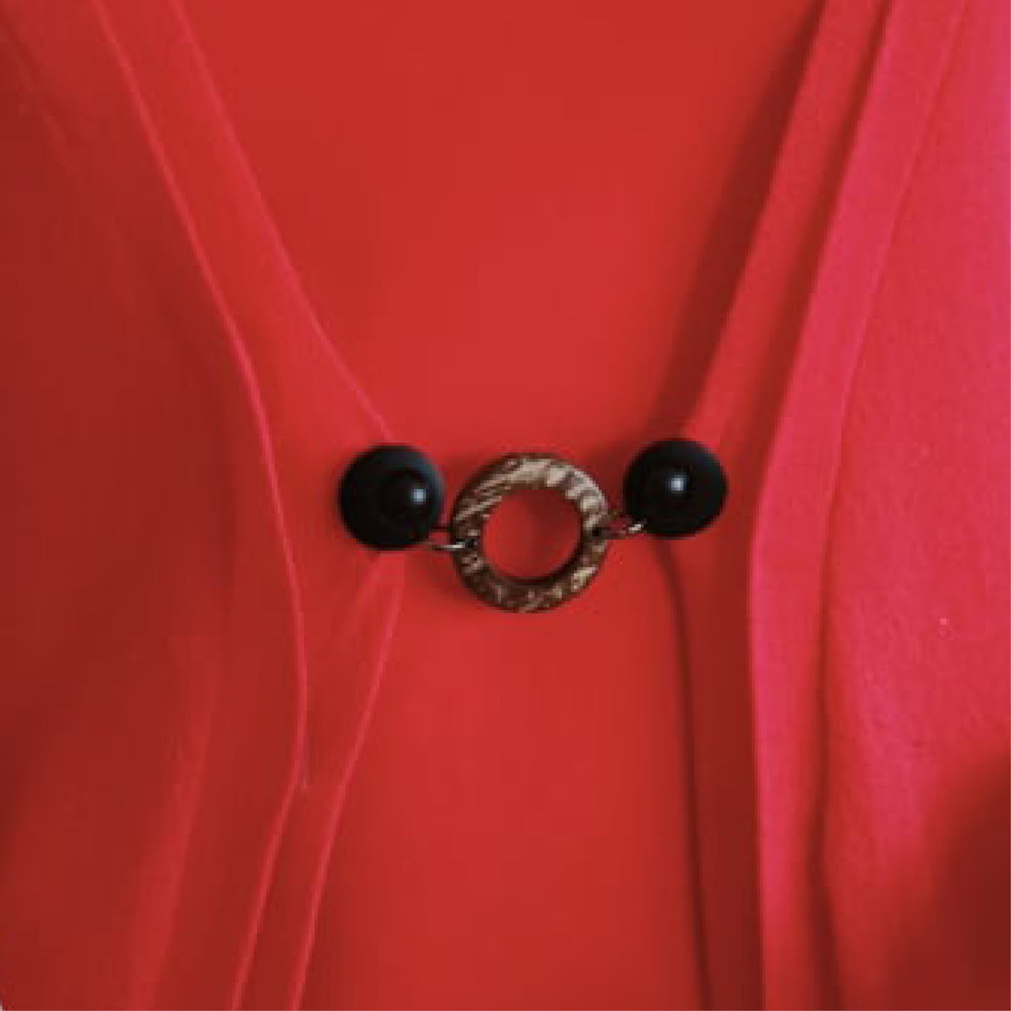 Vestsluiting Kokos zwart in close-up op een rood vest, stijlvolle Fashionclip met zwarte clips en natuurlijke ringvormige tussenbedel.